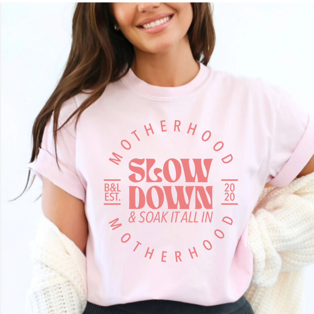 Woman modeling a graphic t-shirt from Branded & Labeled with the phrase “Motherhood: slow down and soak it all in” printed on the front, styled for a relaxed, everyday look
