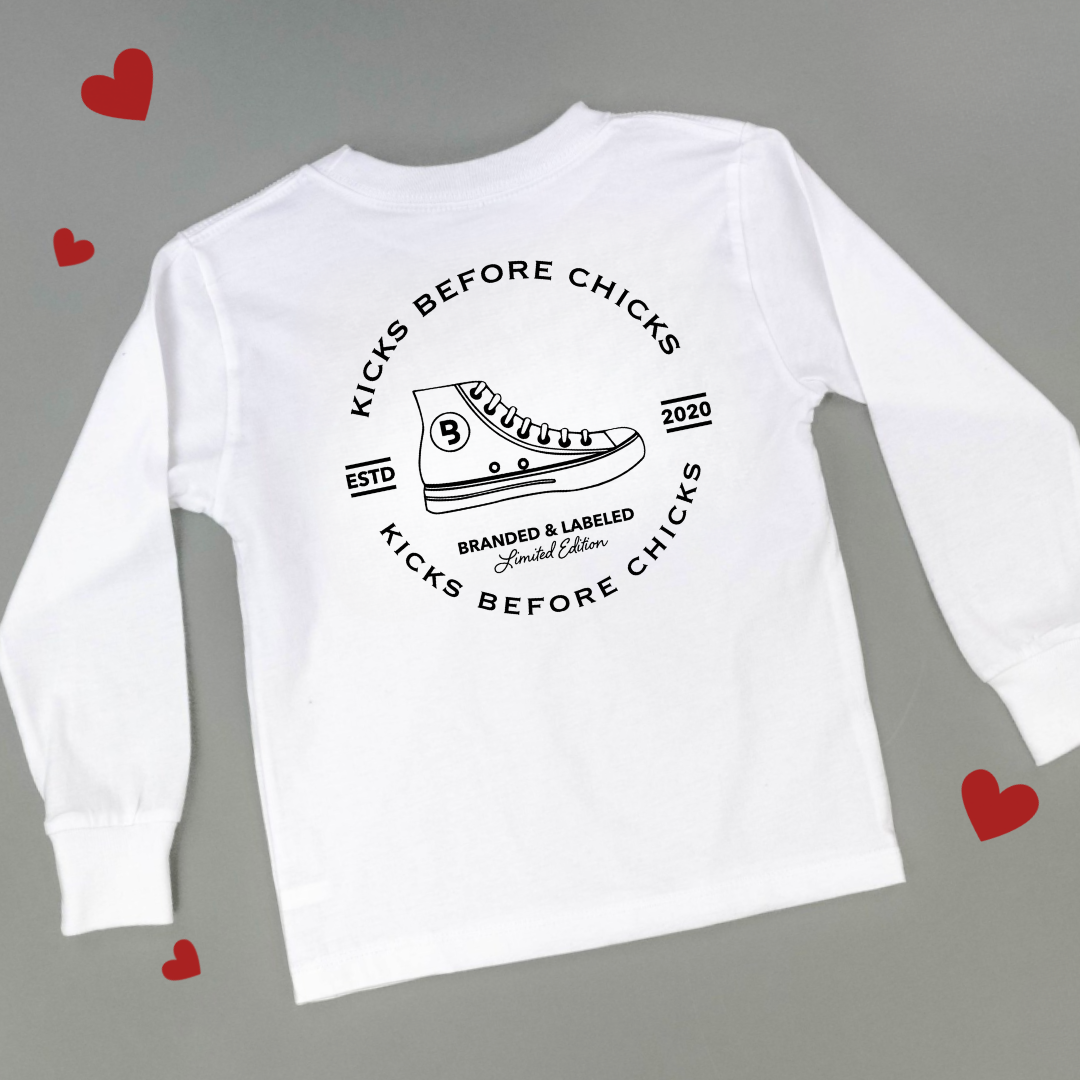White kids long sleeve shirt featuring a large ‘Kicks Before chicks’ graphic printed on the back