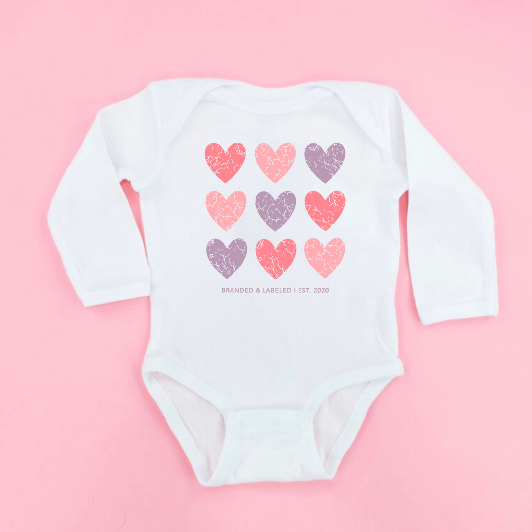 Infant white long sleeve onesie featuring the “Loved Over Time” design with distressed hearts in light pink, purple, and dark pink tones on the front.