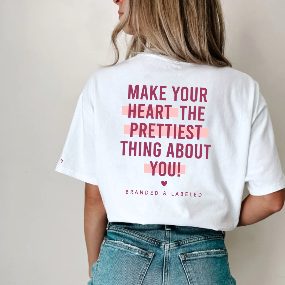 Woman wearing a white short sleeve shirt, shown from the back, featuring the “make your heart the prettiest thing about you” graphic design printed on the back.