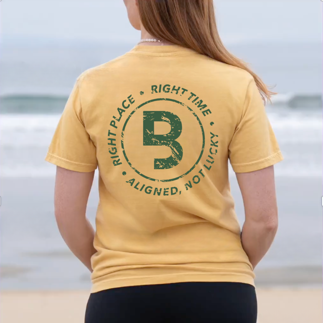 WOMAN AT THE BEACH MODELING THE BACK OF A SHIRT THAT SAYS RIGHT PLACE, RIGHT TIME, ALIGNED NOT LUCKY
