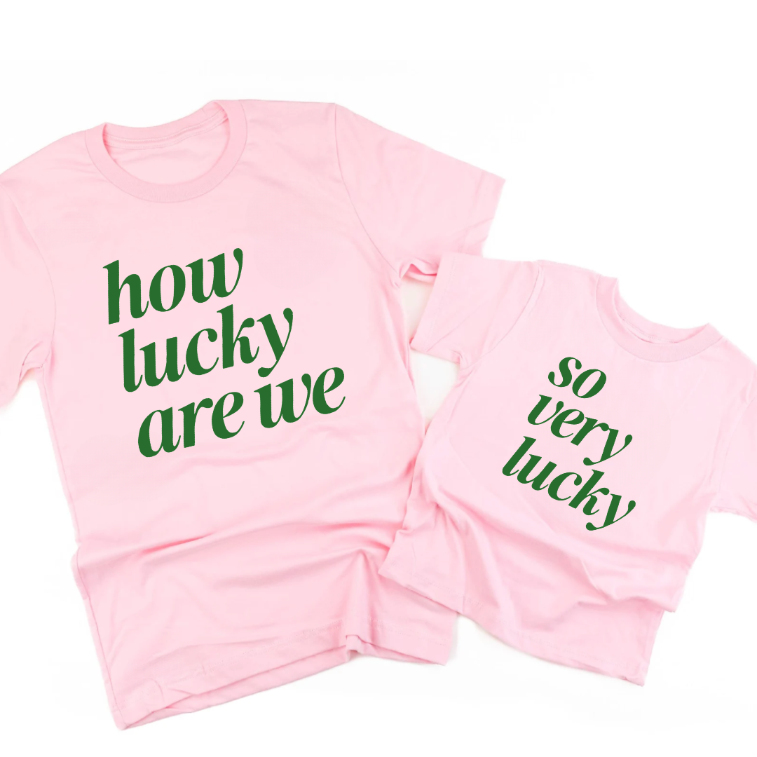 matching set of 2 - one adult and one kids tee laying side by side with the adult tee saying "How Lucky Are We" and the kids tee saying "So Very Lucky"