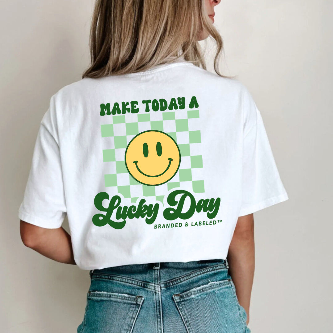 Woman modeling a white tshirt with "Make Today A Lucky Day" printed in the back with a smiley face graphic thats positioned infront of a lightgree checkered background