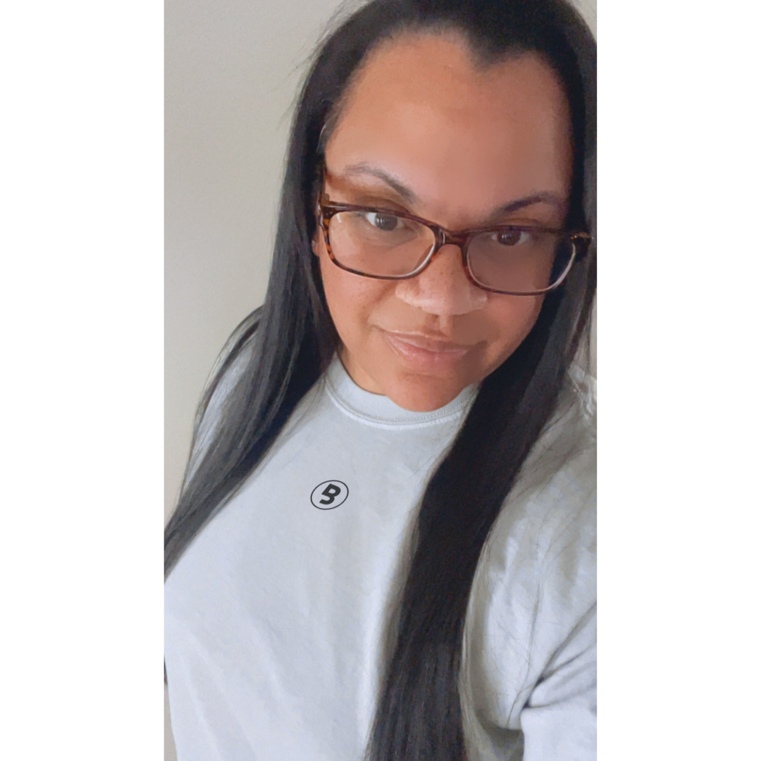Woman wearing glasses while modeling a bay colored premium tee with the signature Branded & Labeled "B" logo printed in black located center chest near collar