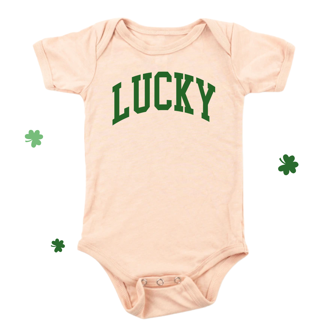 Peach infant bodysuit with ‘Lucky’ printed in green lettering on the front.