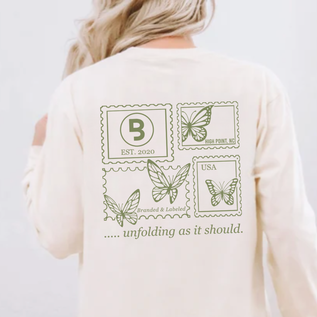 woman modeling the back of a shirt with a series of stamps with butterflies and text and underneath it reads ".... unfolding as it should"