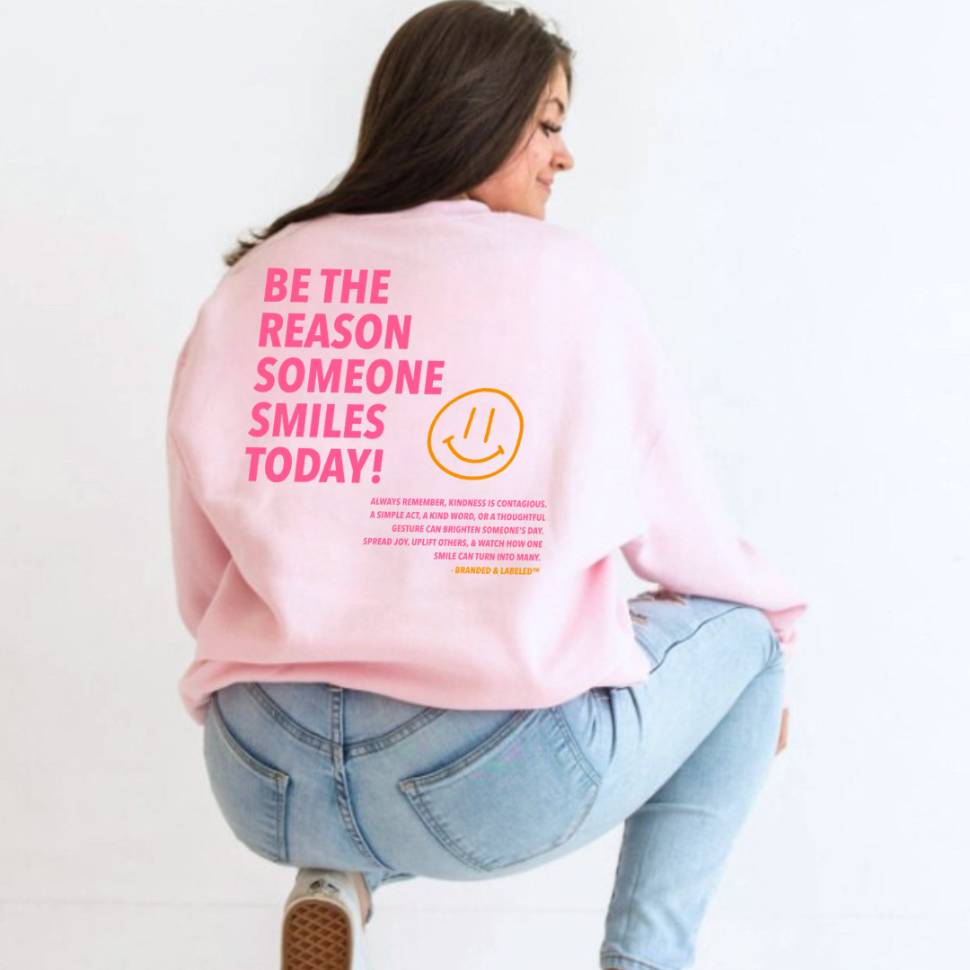 Woman wearing a fleece pullover showing the back design that reads “Be the Reason Someone Smiles Today” with an inspirational kindness message and subtle Branded & Labeled text underneath.