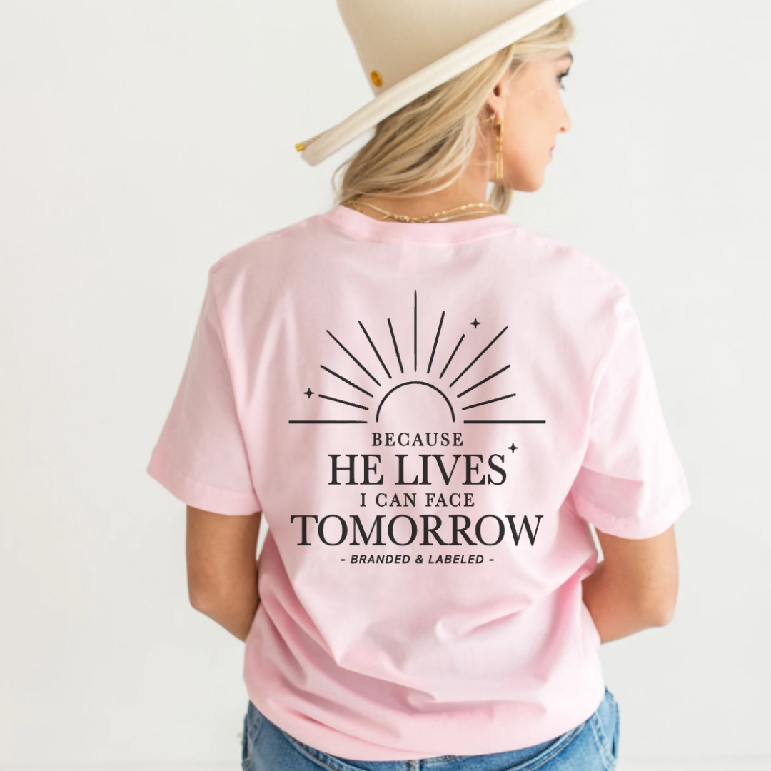 Woman wearing a premium tee featuring the back design “Because He Lives I Can Face Tomorrow” with small “Redeemed” text printed on the front chest from Branded & Labeled.