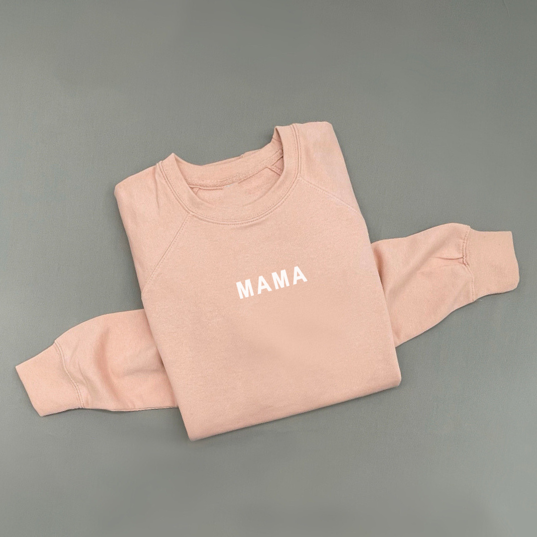 Flat lay of a luxe terry crew sweatshirt featuring a subtle “MAMA” detail printed near the collar, shown in a clean, minimal presentation.