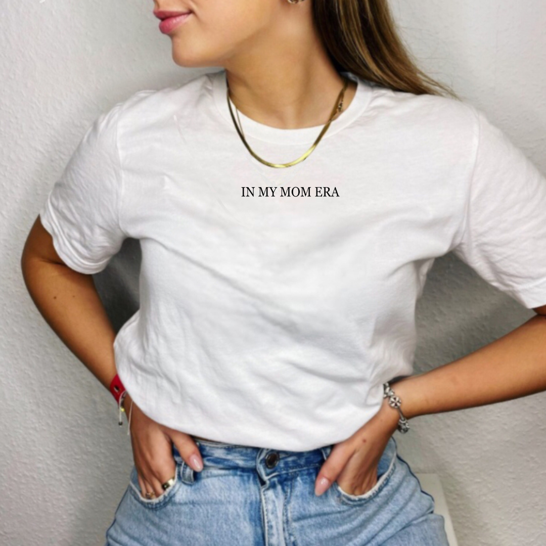 Woman modeling an adult everyday tee featuring subtle “In My Mom Era” text in a refined font, printed at the center chest near the collar from Branded & Labeled