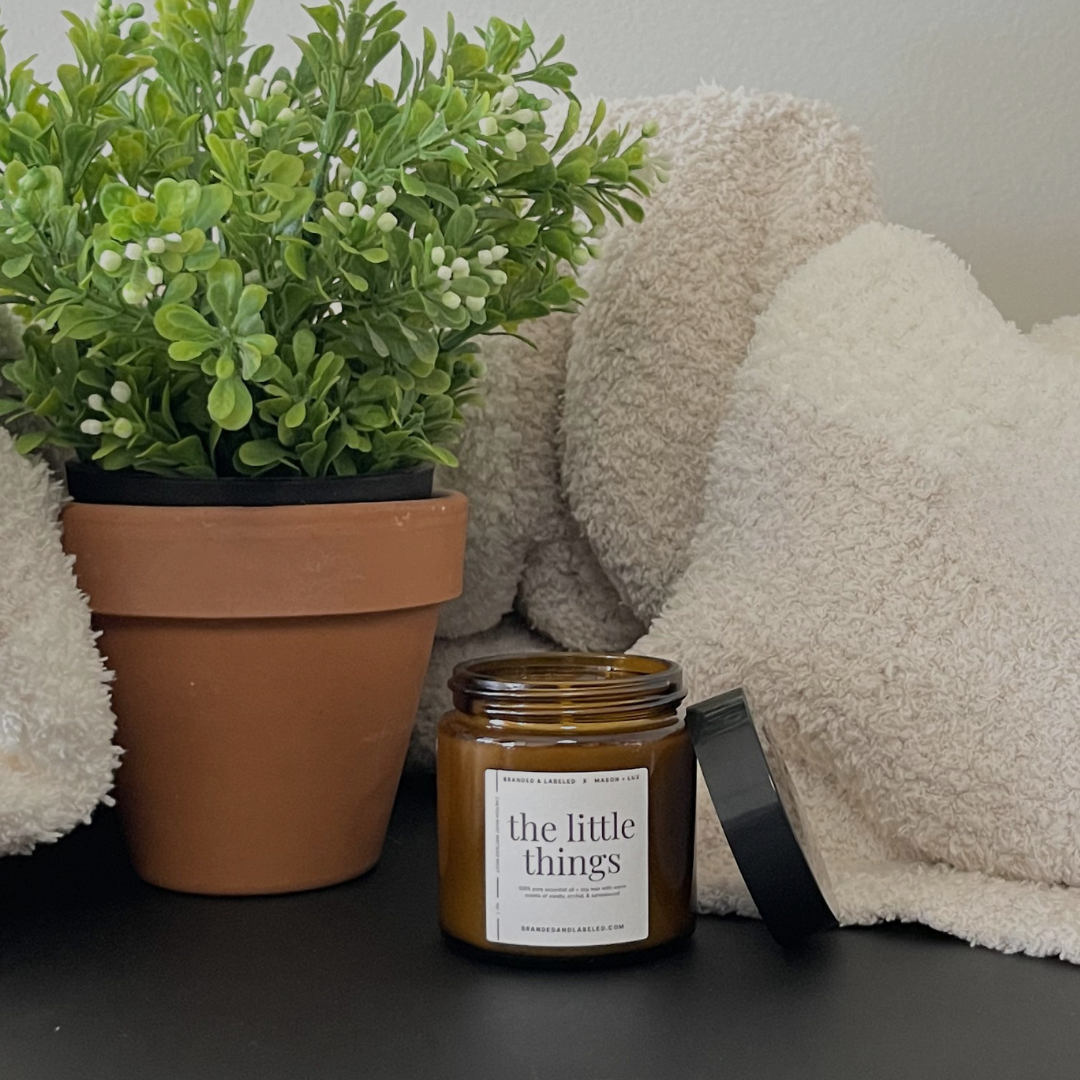 4oz Branded & Labeled soy candle displayed with a plant and a blanket, creating a warm and cozy lifestyle setting.