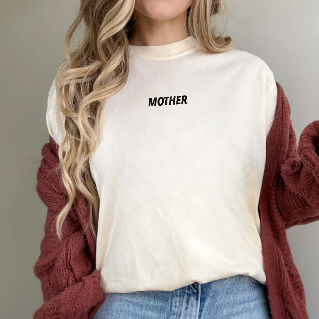 Woman modeling an adult premium tee featuring subtle “MOTHER” text in a small all-caps font, printed at the center chest near the collar from Branded & Labeled