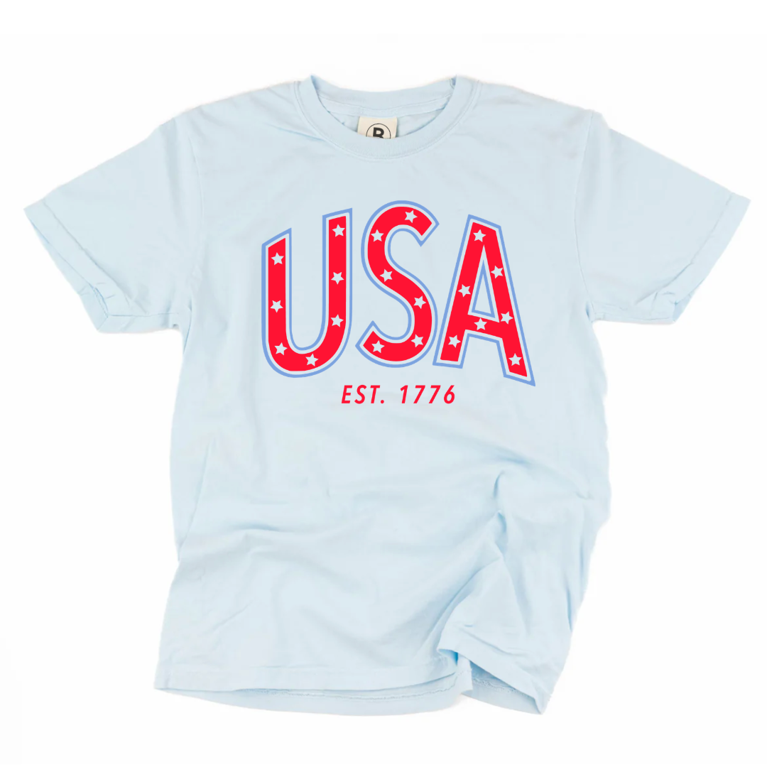 Premium adult graphic tee featuring bold “USA” typography with est. 1776 detail in red and blue patriotic colors, part of the American Classics Collection by Branded & Labeled.