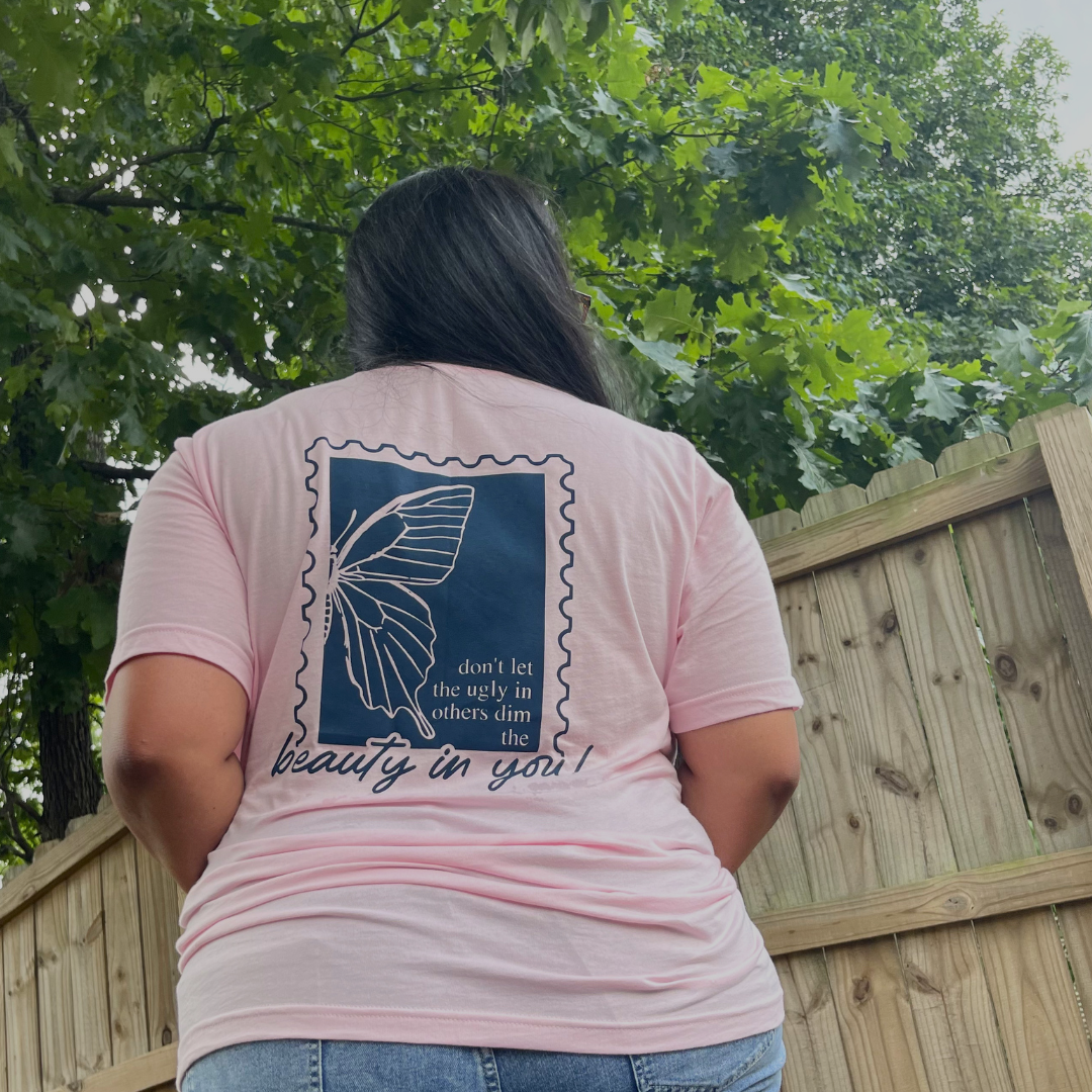 Woman modeling the Beauty in You adult Everyday Tee, featuring a large butterfly graphic and inspirational message on the back with Branded & Labeled printed on the front left chest.