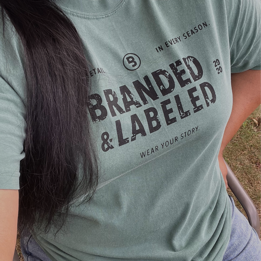 Woman modeling The Storyline adult premium tee featuring the message “In every detail. In every season. Wear your story.” with Branded & Labeled centered in the design.