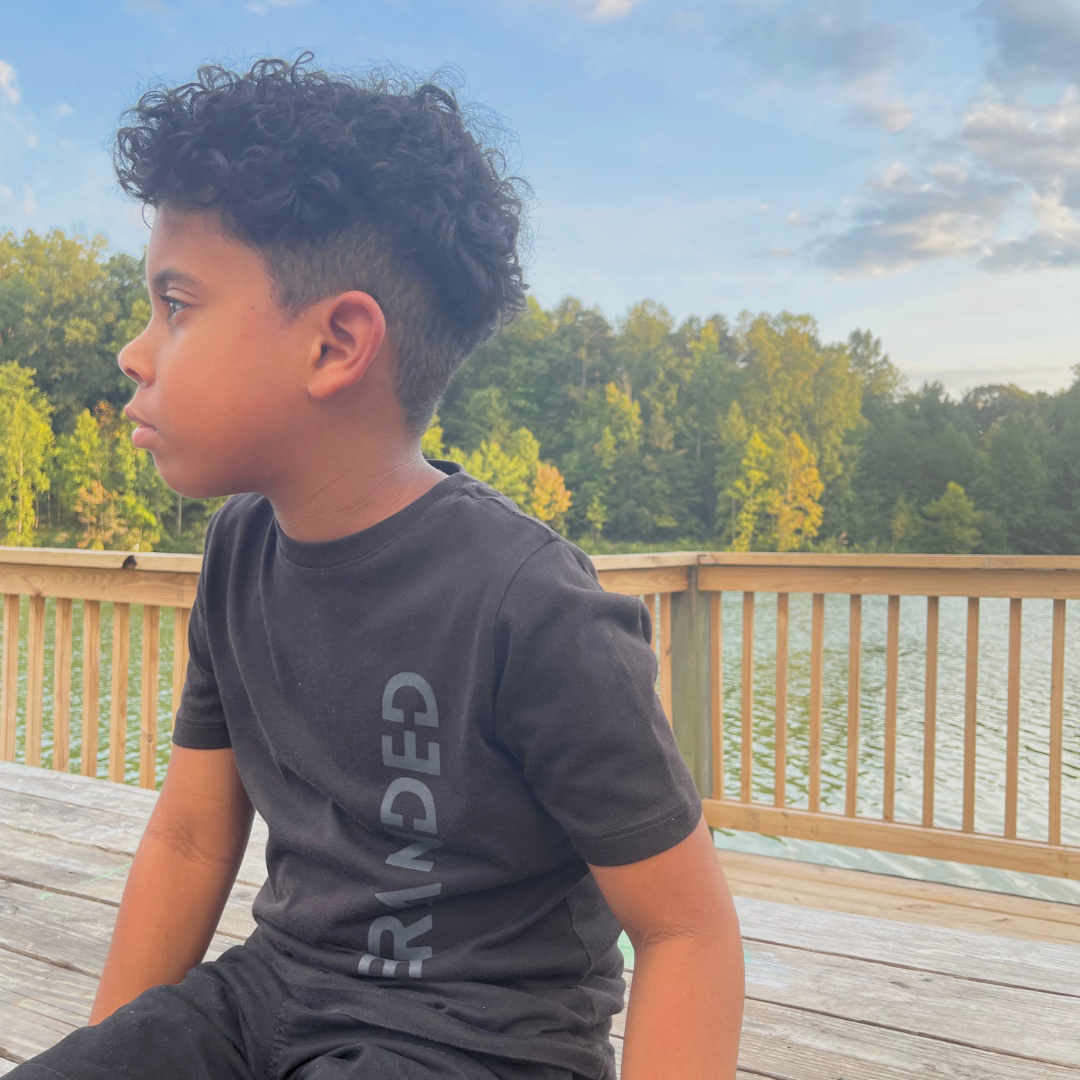Child wearing the Black Label Kids Tee in black, featuring a subtle dark gray BRANDED graphic running down the side for a monochromatic look.