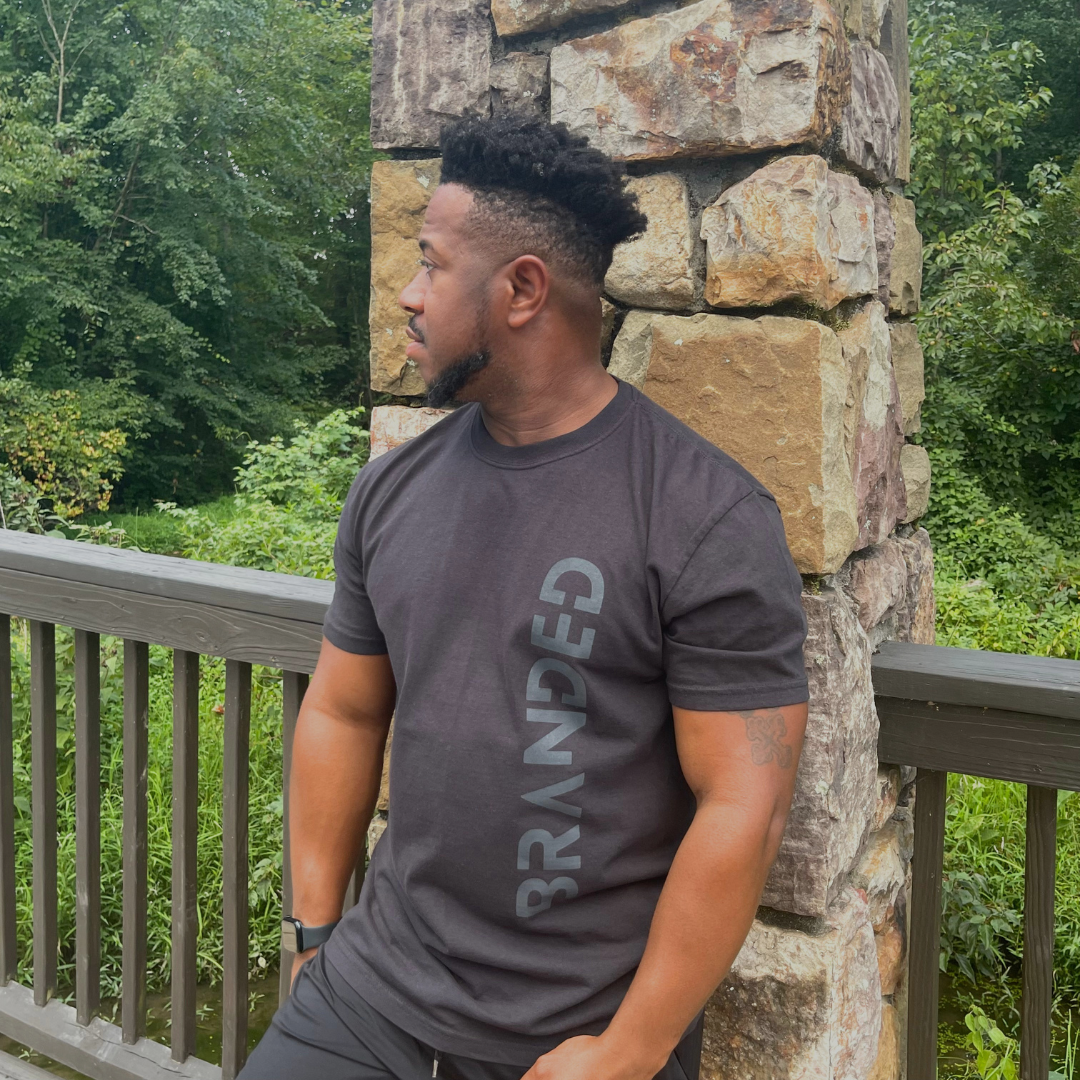 Adult wearing the Black Label Premium Tee in black, featuring a dark gray BRANDED graphic running down the side for a subtle monochromatic look.
