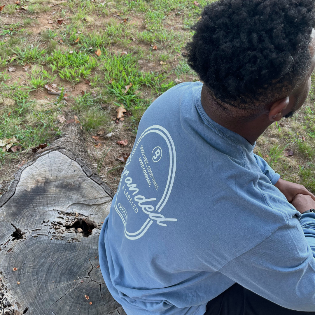Man wearing the Good Company Adult Premium Long Sleeve, a unisex graphic shirt featuring Good Vibes Good Times Good Company on the front and a large oval Branded & Labeled Since 2020 design on the back.