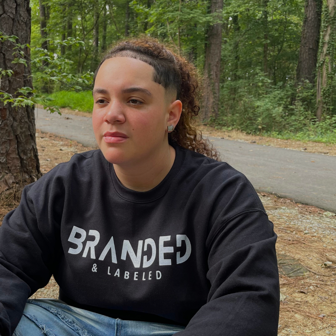 Woman outside wearing the Onyx Fleece Pullover, a black fleece sweatshirt with the Branded & Labeled logo printed in white across the front.