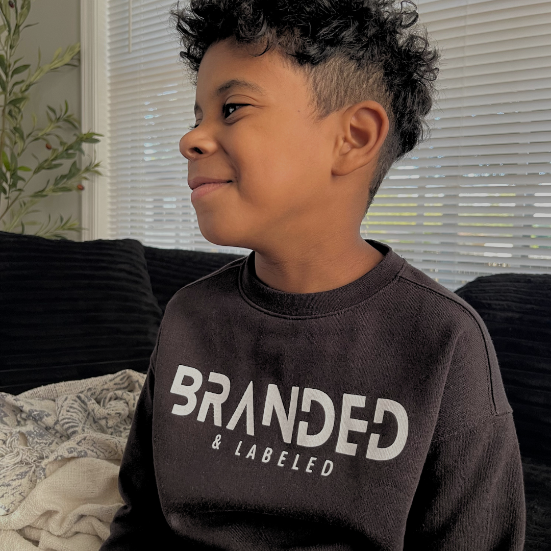 Boy wearing the Kids Onyx Fleece Pullover, a black youth fleece sweatshirt featuring the Branded & Labeled logo printed in white across the front.