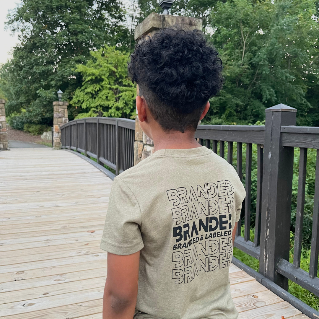 Kid wearing The Imprint Kids Tee with a bold Branded & Labeled repeated design printed down the back