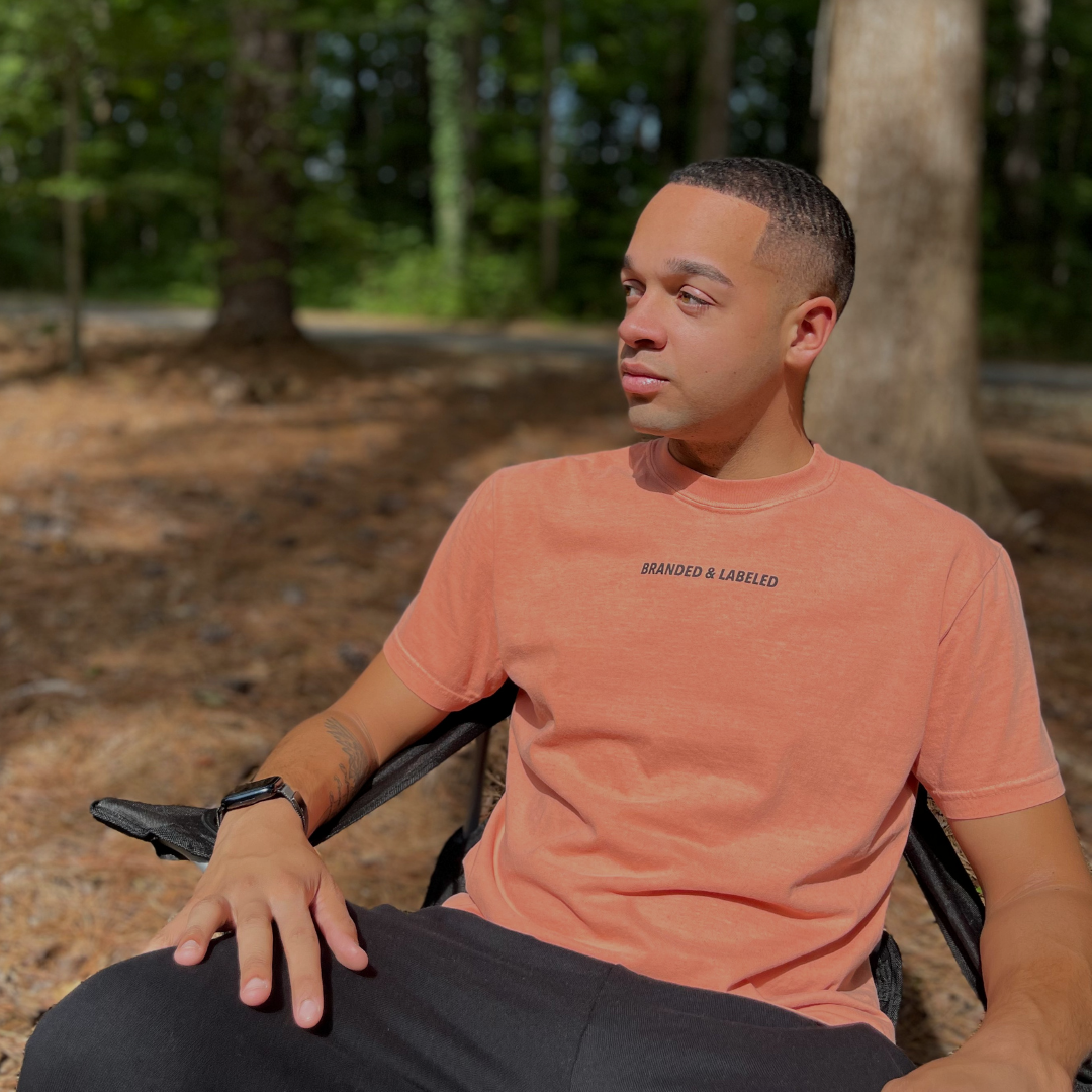 Adult wearing The Label Premium Tee from Branded & Labeled, a garment-dyed graphic t-shirt with subtle Branded & Labeled lettering printed near the collar.